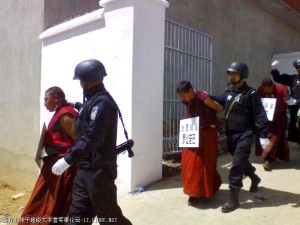 Reminiscent of the Cultural Revolution, at three least monks with placards around their necks are lead away from their monastery by armed security personnel. Reminiscent of the Cultural Revolution, at three least monks with placards around their necks are lead away from their monastery by armed security personnel.